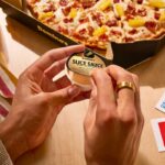 This photo shows a woman's hands unsealing a cup containing Domino's Slice Sauce.
