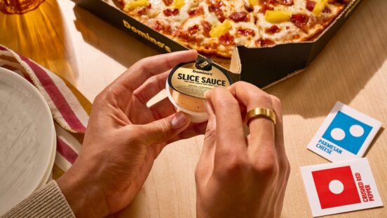This photo shows a woman's hands unsealing a cup containing Domino's Slice Sauce.