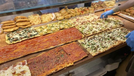 This photo shows a display case featuring various Roman-style pizzas waiting to be served.