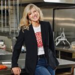 This photo shows Jane Grote Abell smiling and posing in the kitchen of a Donatos Pizza location.
