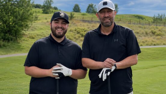 This photo shows Jerry Flores on the left and Gerardo Flores on the right, both standing on a golf course, wearing golf attire and holding golf clubs while looking at the camera.
