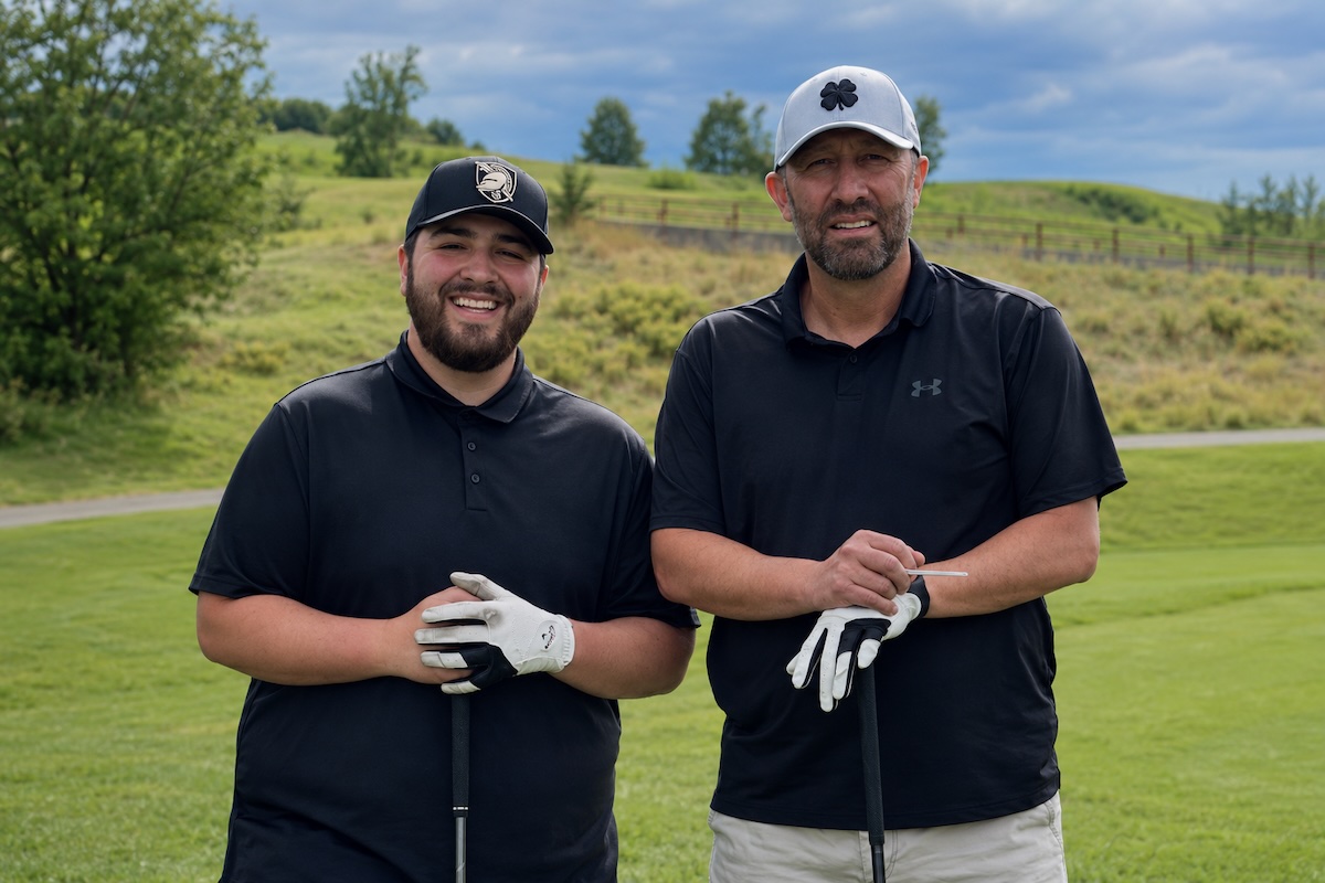 This photo shows Jerry Flores on the left and Gerardo Flores on the right, both standing on a golf course, wearing golf attire and holding golf clubs while looking at the camera.
