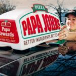 This photo shows a female driver for Papa Johns putting the car toppers sign on her car.