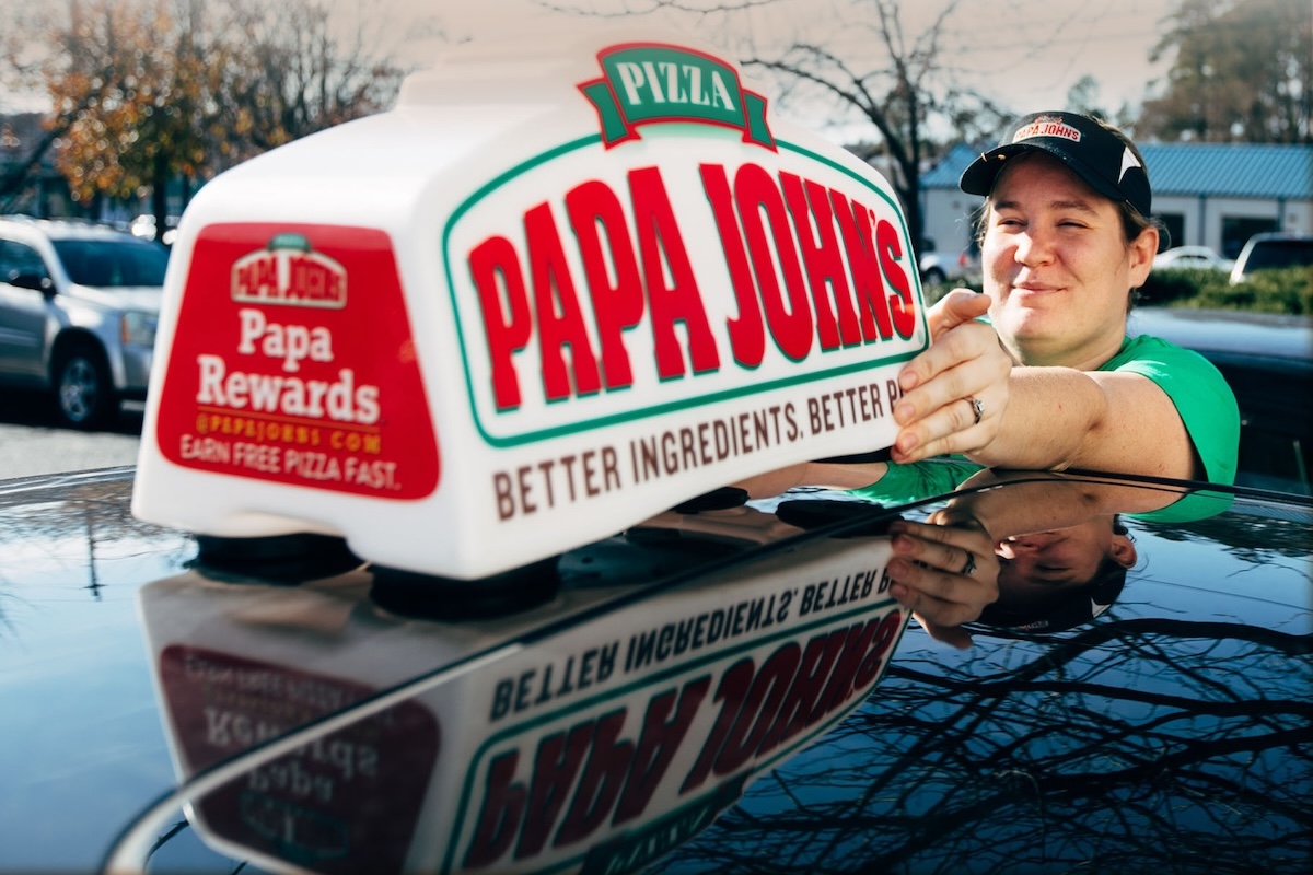 This photo shows a female driver for Papa Johns putting the car toppers sign on her car.
