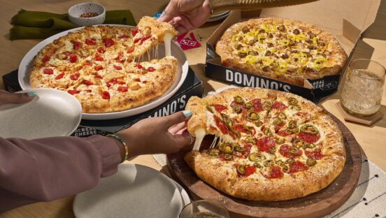 This photo shows customers' hands reaching for different slices of several pizzas from Domino's.