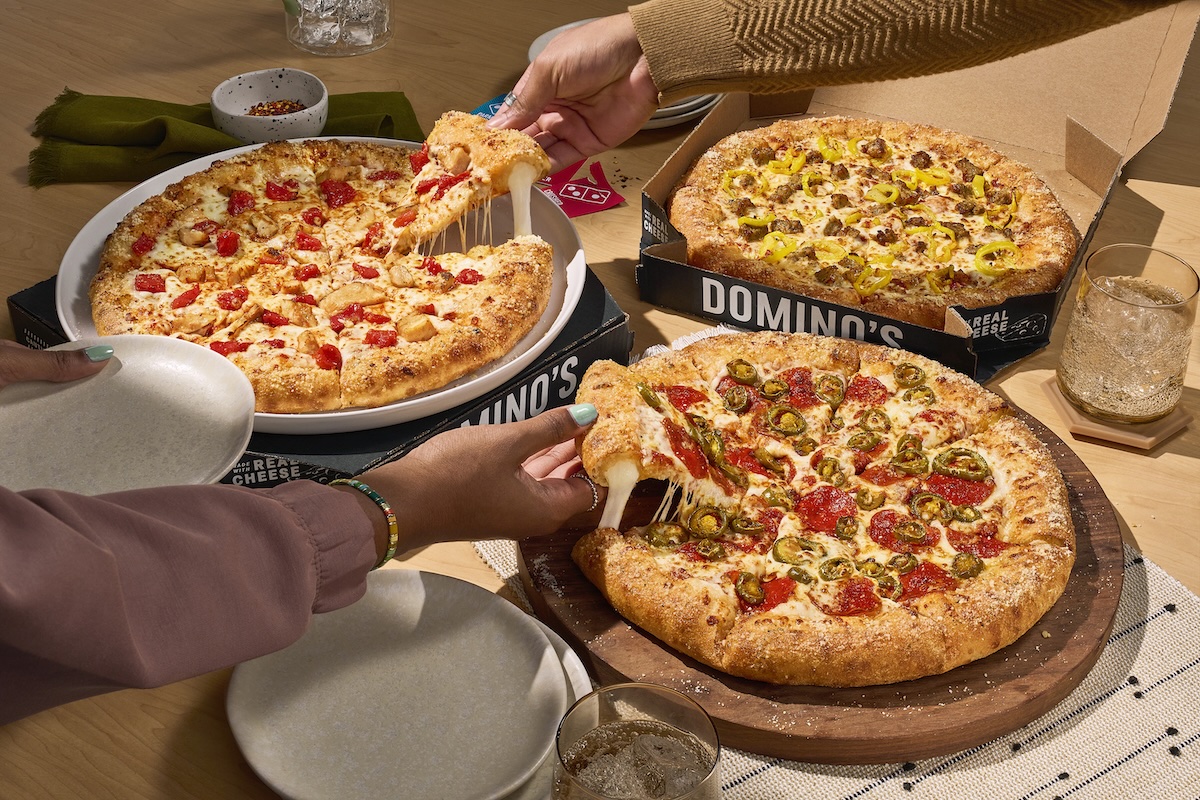 This photo shows customers' hands reaching for different slices of several pizzas from Domino's.