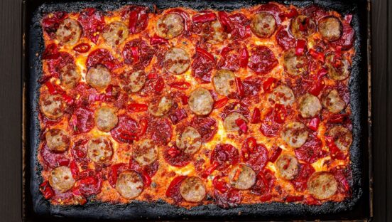 This photo shows a pizza topped with beef pepperoni, sausage, pepperoni bites, hot peppers and other toppings.