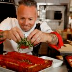 This photo shows Tony Gemignani leaning in closely and adding arugula to a Detroit-style pizza.
