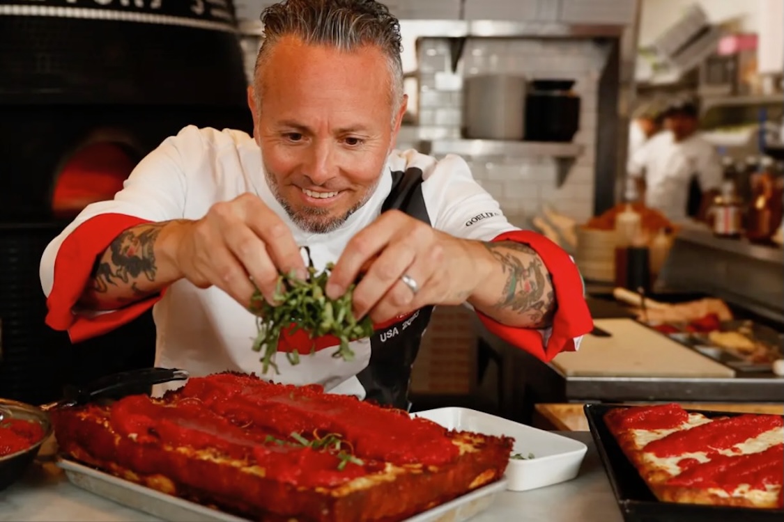 This photo shows Tony Gemignani leaning in closely and adding arugula to a Detroit-style pizza.