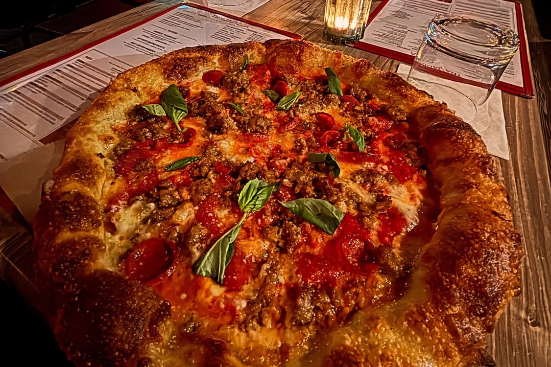 This photo shows a round pizza with a thick cornicione topped with sausage and pepperoni.