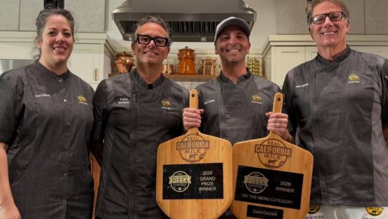 This photo shows contest winner Zac Calder holding his two pizza peel trophies and standing with the competition judges.