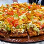 This photo shows a pizza topped with seasoned beef, lettuce, sliced tomatoes and corn chips.