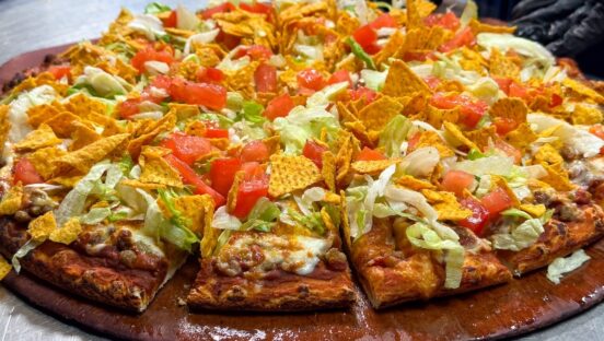 This photo shows a pizza topped with seasoned beef, lettuce, sliced tomatoes and corn chips.