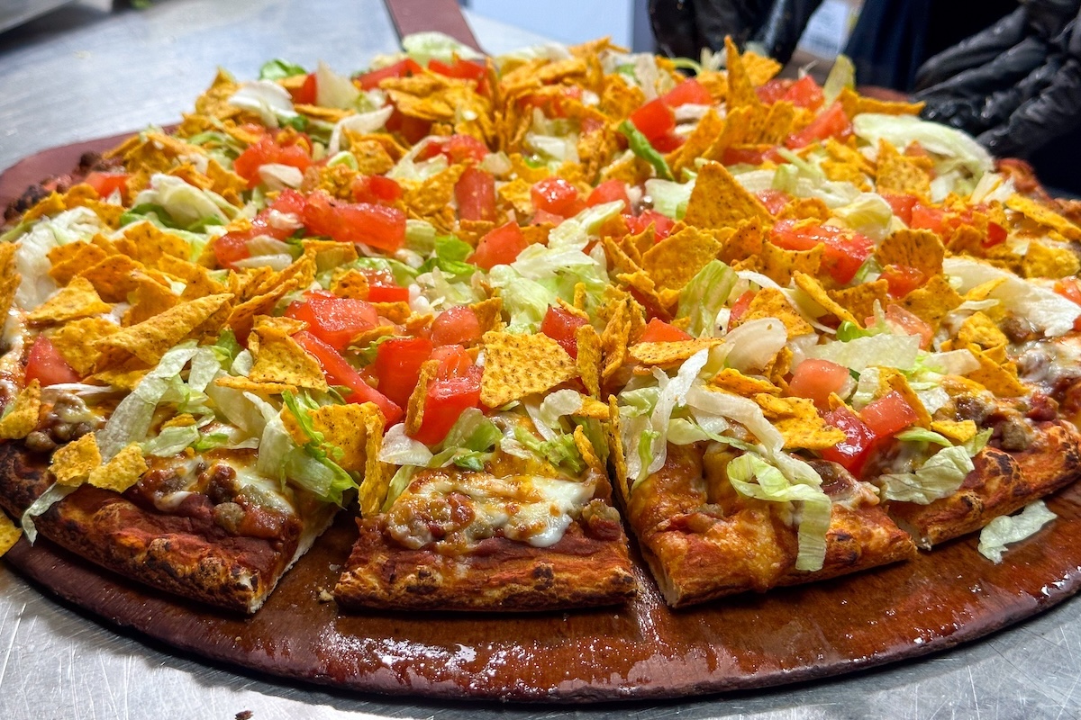This photo shows a pizza topped with seasoned beef, lettuce, sliced tomatoes and corn chips.