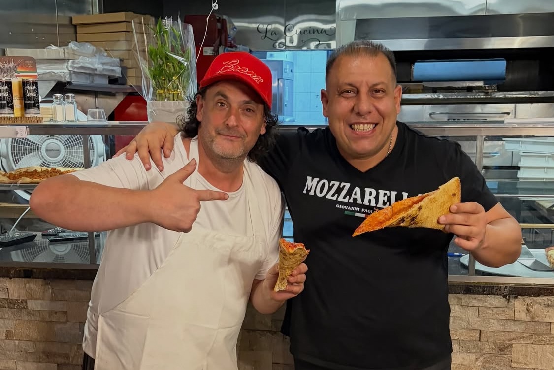 This photo shows Daniel Romano giving the thumbs-up while a friend puts his arm around him and enjoys a slice of pizza.
