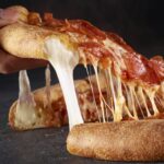 This photo shows someone's hand removing a slice of pizza, with cheese oozing out of the crust, of Papa Johns' Epic Stuffed Crust Pizza.