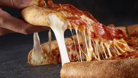 This photo shows someone's hand removing a slice of pizza, with cheese oozing out of the crust, of Papa Johns' Epic Stuffed Crust Pizza.