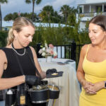 This photo shows a Palm Beach Mobile employee in a black dress serving caviar to a female customer in a yellow dress in an outdoor setting.