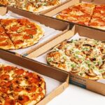 This photo shows an array of different types of pizza in carryout boxes.