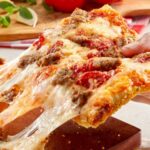 This photo shows a woman's hand pulling a slice of the chunky sausage pizza from a whole pie.