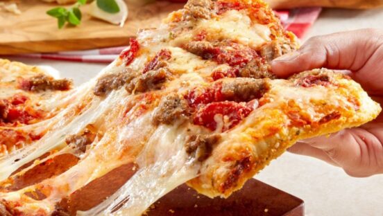 This photo shows a woman's hand pulling a slice of the chunky sausage pizza from a whole pie.