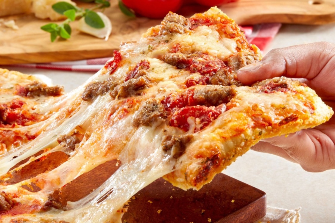 This photo shows a woman's hand pulling a slice of the chunky sausage pizza from a whole pie.