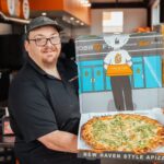 This photo shows Nick Sanford holding up a pizza in the Pizza Bib box.