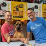 This photo shows the two Protest Pizza owners in their restaurant with a handsome brown dog between them.