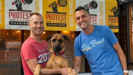 This photo shows the two Protest Pizza owners in their restaurant with a handsome brown dog between them.