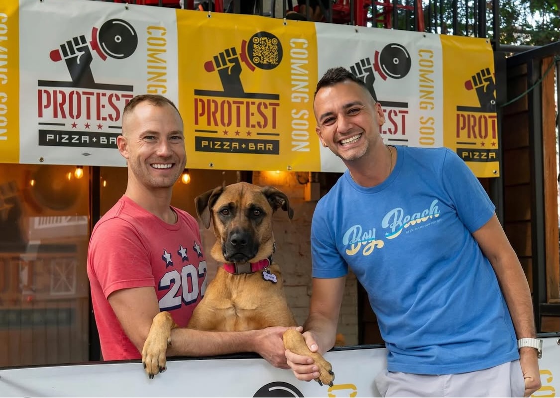 This photo shows the two Protest Pizza owners in their restaurant with a handsome brown dog between them.