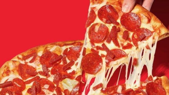 This photo shows a slice being removed from a whole pepperoni pizza with a nice cheese pull. It's set against a red background.
