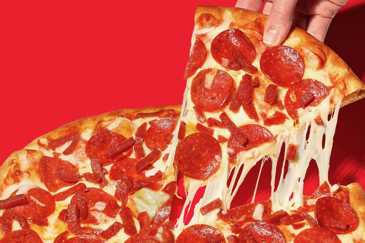 This photo shows a slice being removed from a whole pepperoni pizza with a nice cheese pull. It's set against a red background.