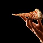 This photo shows a Hand holding slice of cheese pizza cut in slices