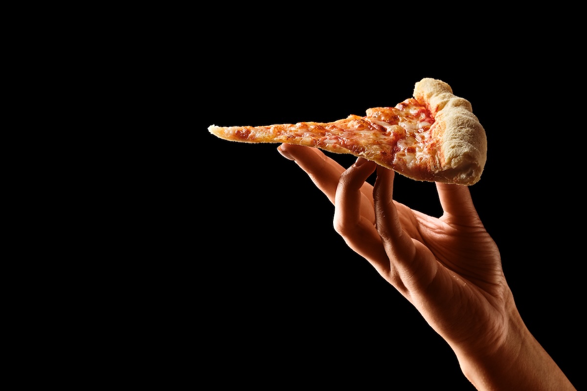 This photo shows a Hand holding slice of cheese pizza cut in slices