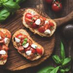 This photo depicts Italian bruschetta antipasti with tomatoes, mozzarella cheese and basil on a wooden board.