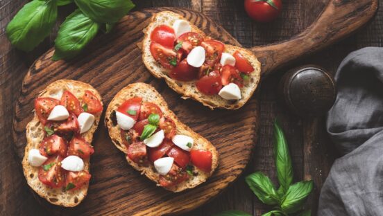 This photo depicts Italian bruschetta antipasti with tomatoes, mozzarella cheese and basil on a wooden board.