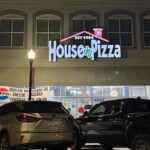 This photo shows the exterior of the House of Pizza, including a new sign and cars in the parking lot.