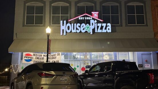 This photo shows the exterior of the House of Pizza, including a new sign and cars in the parking lot.
