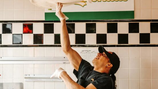 This photo shows a man spinning a round disc of dough high above his head.
