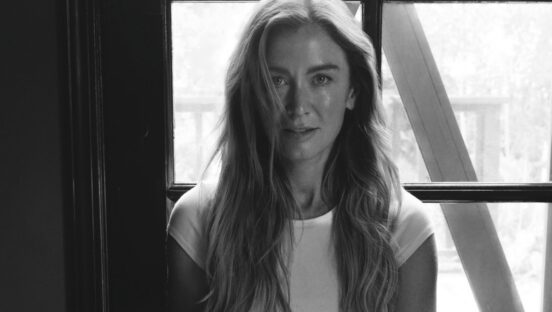 This black-and-white photo shows Katie sitting in the lotus position in front of a window with a pen and notebook in her hands.