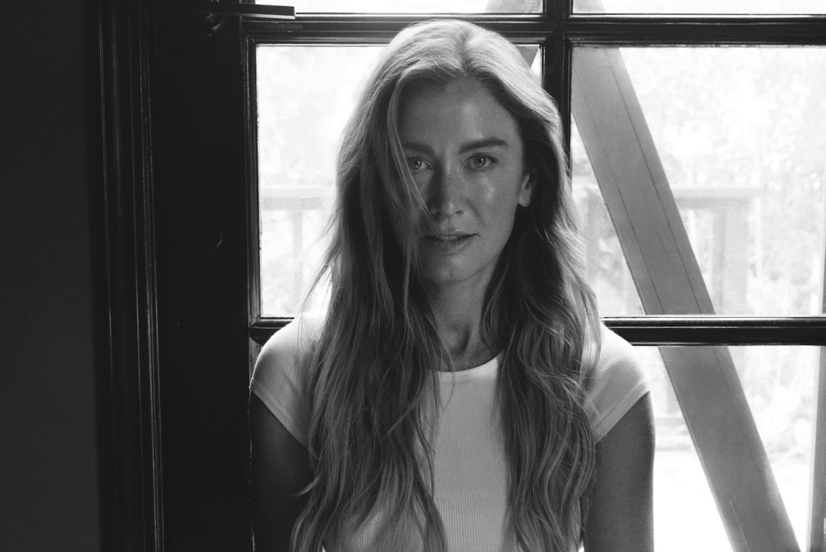 This black-and-white photo shows Katie sitting in the lotus position in front of a window with a pen and notebook in her hands.