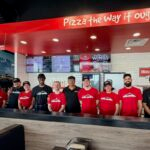 This photo shows a group of employees standing behind the ordering counter at a new location of Mountain Mike's Pizza.