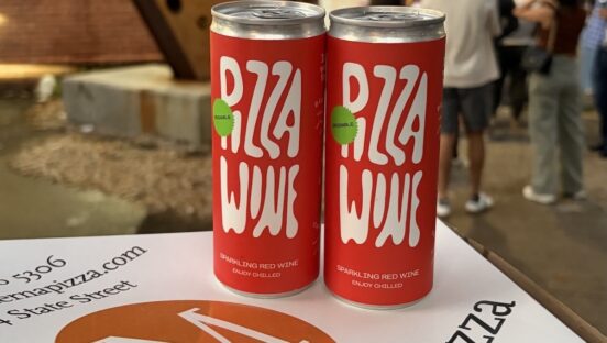 This photo shows two cans of Pizza Wine (red with white lettering) sitting on a Modern Apizza pizza box.