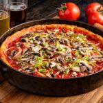 This photo shows a deep-dish pizza in the pan. It's topped with mushrooms and green bell peppers.