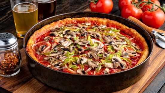 This photo shows a deep-dish pizza in the pan. It's topped with mushrooms and green bell peppers.