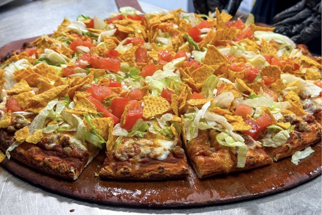 This photo shows the taco pizza from Happy Joe's, topped with ground beef, lettuce, tomatoes, cheese and corn chips.