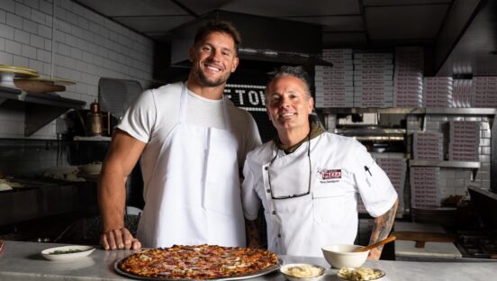 This photo shows Nick Bosa and Tony Gemignani smiling and standing side by side with The Boss pizza placed in front of Bosa.