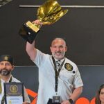 This photo shows Vito Recchia, wearing a white chef coat, holding his trophy in the air at the Pizza Champion Cup International.