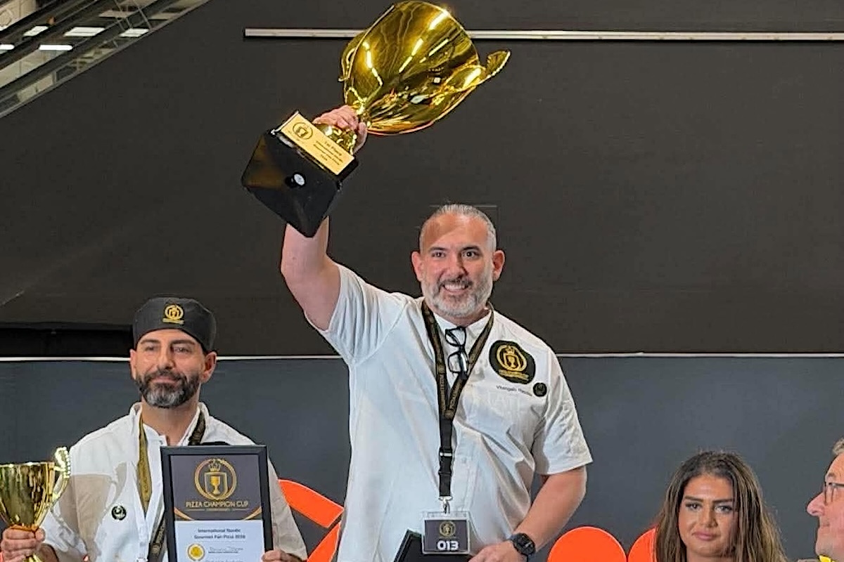 This photo shows Vito Recchia, wearing a white chef coat, holding his trophy in the air at the Pizza Champion Cup International.