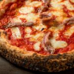 This photo shows a pizza with tomato, mozzarella and anchovies.